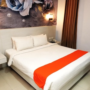 A bed with white bedding and an orange accent, a nightstand with a phone, and a wall with a floral mural. - Halogen Hotel (Sidoarjo)