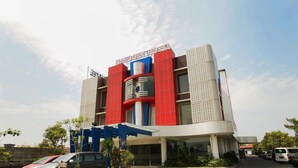 A modern hotel with a prominent red and blue facade, a check-in sign, and a parking area with several cars. - Halogen Hotel (Sidoarjo)