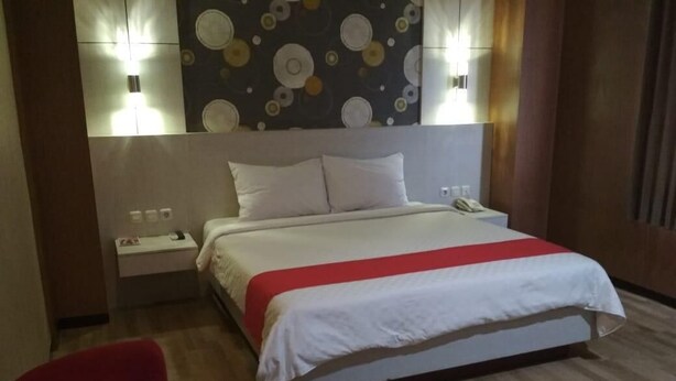 A hotel room with a bed, a nightstand, a red chair, and a wall with circular patterns. - Halogen Hotel (Sidoarjo)