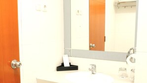 A bathroom with a white sink, a mirror, a towel rack, and a door. - Halogen Hotel (Sidoarjo)