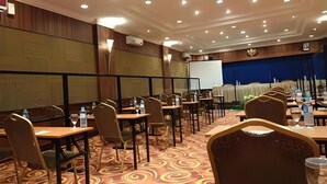 Un salón de conferencias con varias mesas y sillas, una pizarra y una pantalla de proyección.