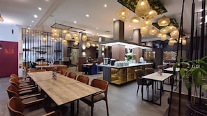 A modern dining area with multiple tables and chairs, a central bar area, and hanging pendant lights.