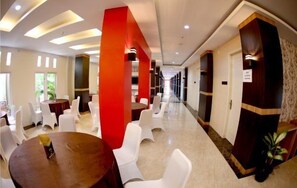 A hotel lobby with round tables and white chairs, red accents on columns, and a long corridor. - Hotel Grand Permata Hati (Banda Aceh)