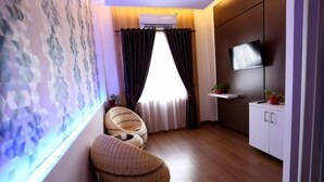 Habitación compacta con un ventanal grande, un televisor de pantalla plana, un mueble pequeño y una silla de fibras naturales.