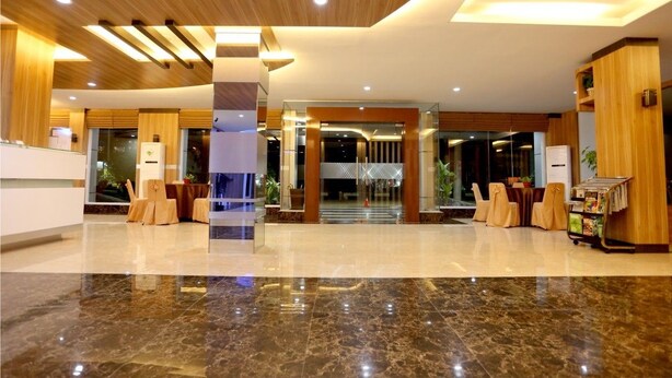 Un moderno vestíbulo de hotel con piso de mármol, detalles de madera y un área de recepción con mostrador y sillones.