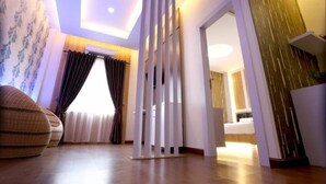 Una habitación de hotel moderna con suelo de madera, un ventanal con cortinas, un sofá y un panel decorativo en la pared.