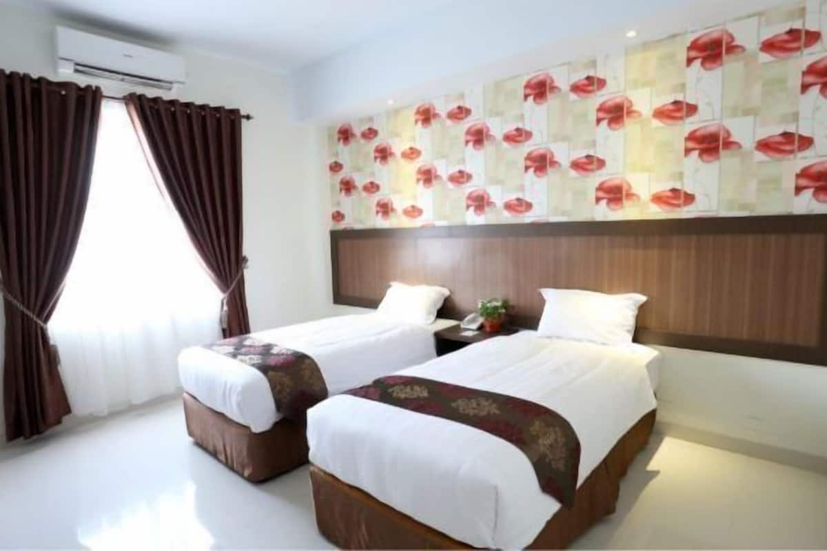 A hotel room with two beds, a large window with curtains, a wall with a floral pattern, and a wooden headboard.