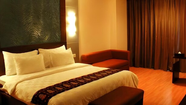 Ein Hotelzimmer mit einem großen Bett, einer kleinen Couch, einem Schreibtisch und einem Vorhang.