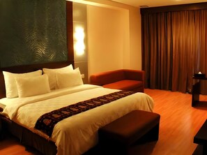 A hotel room with a large bed, a small sofa, a desk, and a curtain.