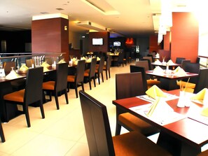 Ein Restaurant mit mehreren Tischen und Stühlen, einige davon mit gelben Servietten und Gläsern.