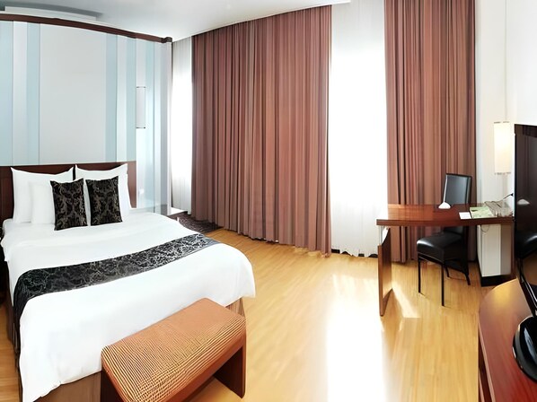 A hotel room with a large bed, a desk with a chair, a television, and a bench.