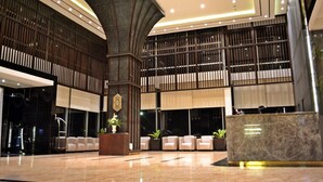 Eine moderne Lobby mit einer zentralen Säule, einer Sitzgelegenheit, einem Empfangsbereich und einer großen Fensterwand.