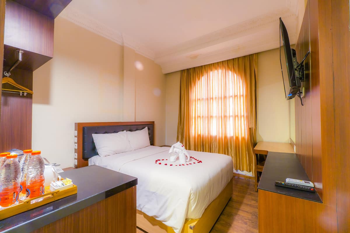 A hotel room with a bed, a desk, a TV mounted on the wall, and a window with curtains.