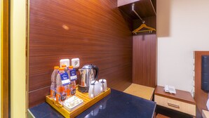 A hotel room with a wooden wall, a wooden counter with a tray of toiletries, a kettle, and a phone on a wooden nightstand. - D'Salvatore Art & Boutique Hotel (Depok)