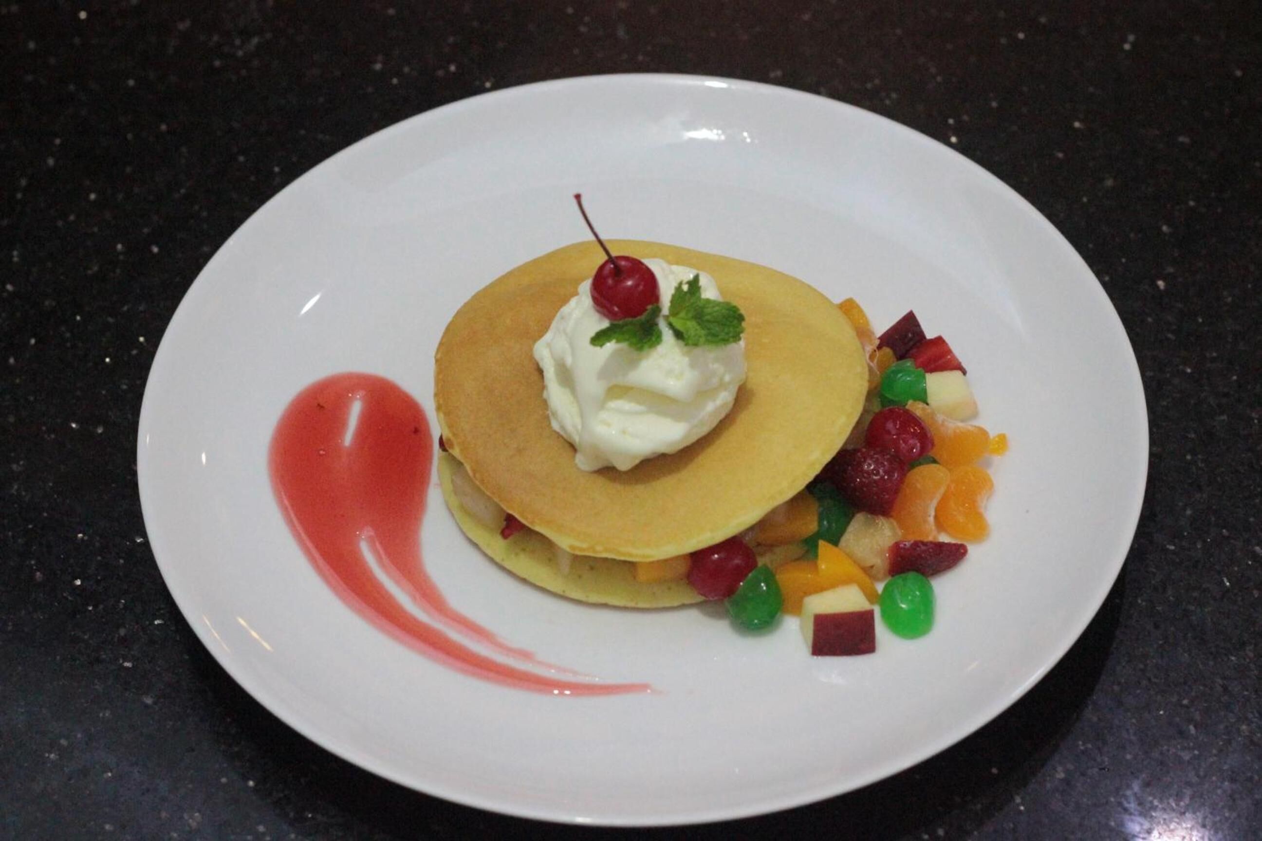 Une assiette avec des crêpes, de la crème fouettée, une cerise et des morceaux de fruits de différentes couleurs.