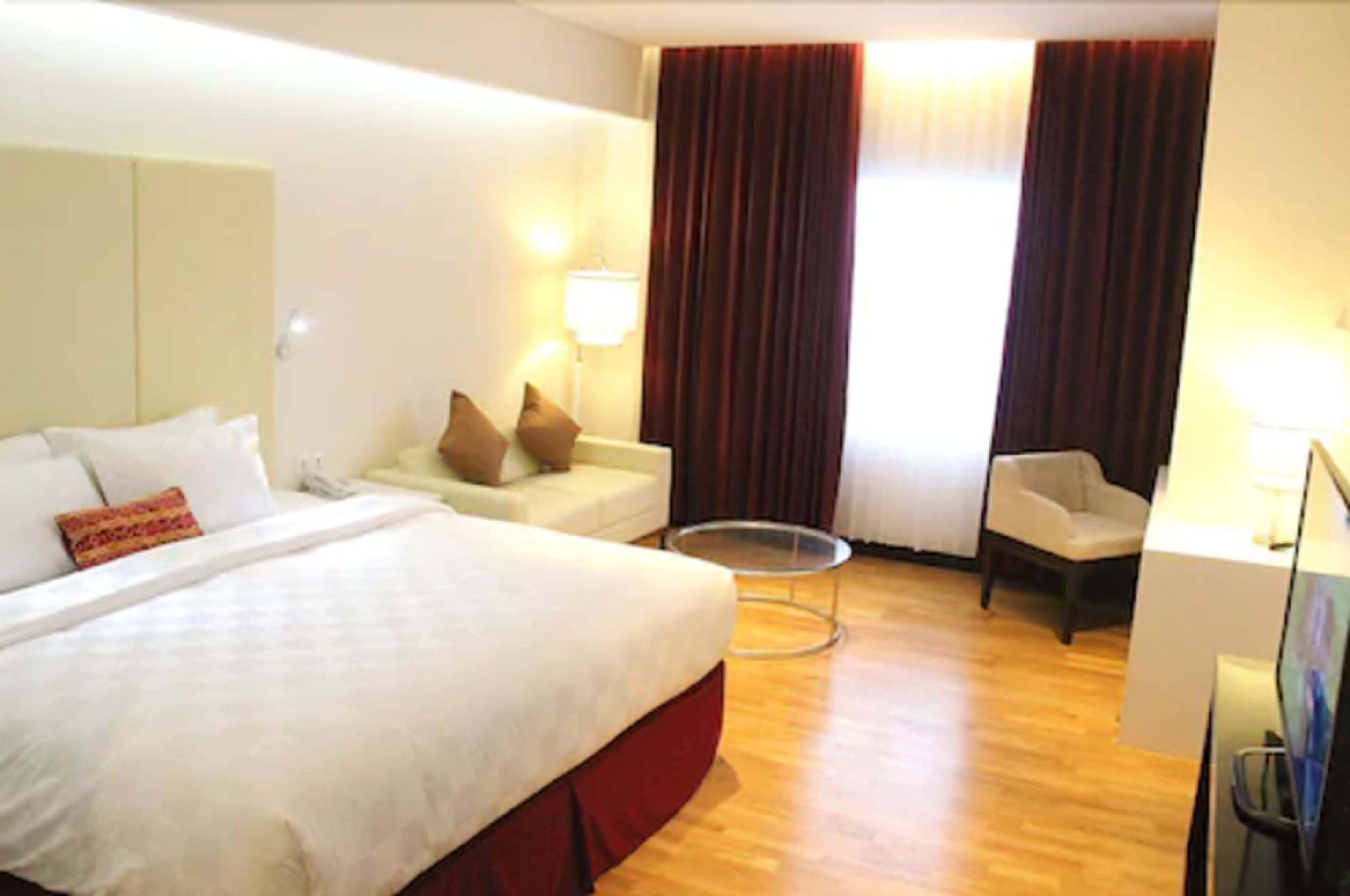 Quarto de hotel com uma cama grande, um sofá pequeno, uma cadeira, uma escrivaninha e uma mesa redonda.