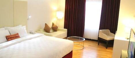 Quarto de hotel com uma cama grande, um sofá pequeno, uma cadeira, uma escrivaninha e uma mesa redonda.
