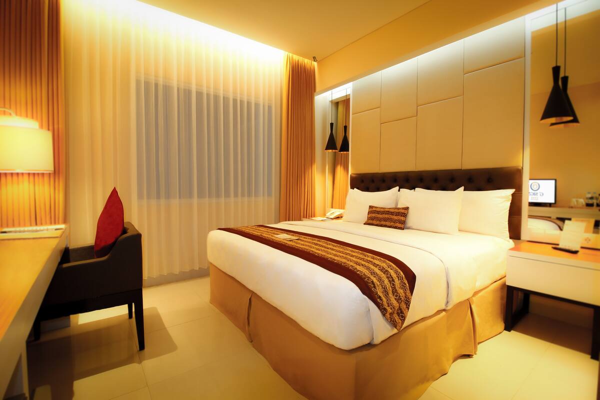 Hotellihuone, jossa on suuri sänky, työpöytä, tuoli ja yöpöytä.