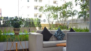 Una sala de estar moderna con un sofá color beige, dos cojines estampados, una mesa de centro de cristal y una pequeña mesa auxiliar de madera.