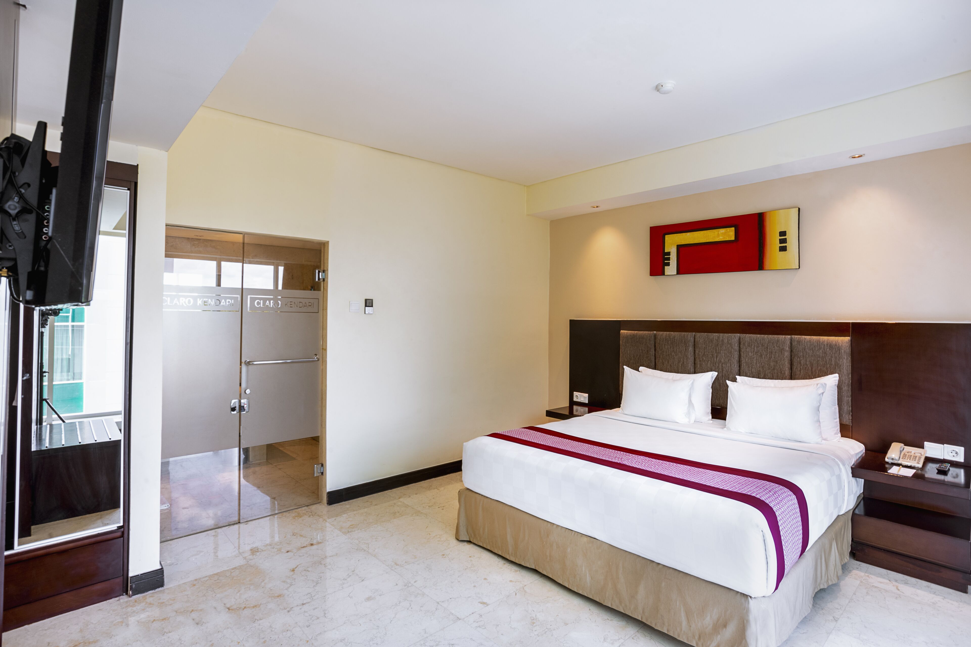 A hotel room with a large bed, a bedside table with a phone, and a modern wall art piece.