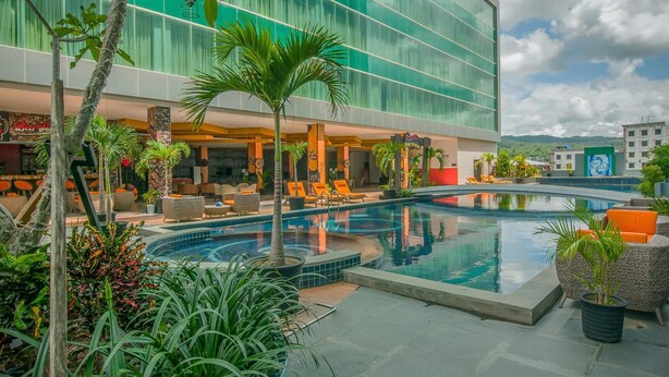 A hotel pool area with a modern building, lounge chairs, and tropical plants. - Claro Kendari (Kendari)
