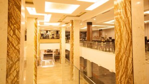 A modern hotel lobby with marble columns, a glass railing, and a central seating area. - Claro Kendari (Kendari)