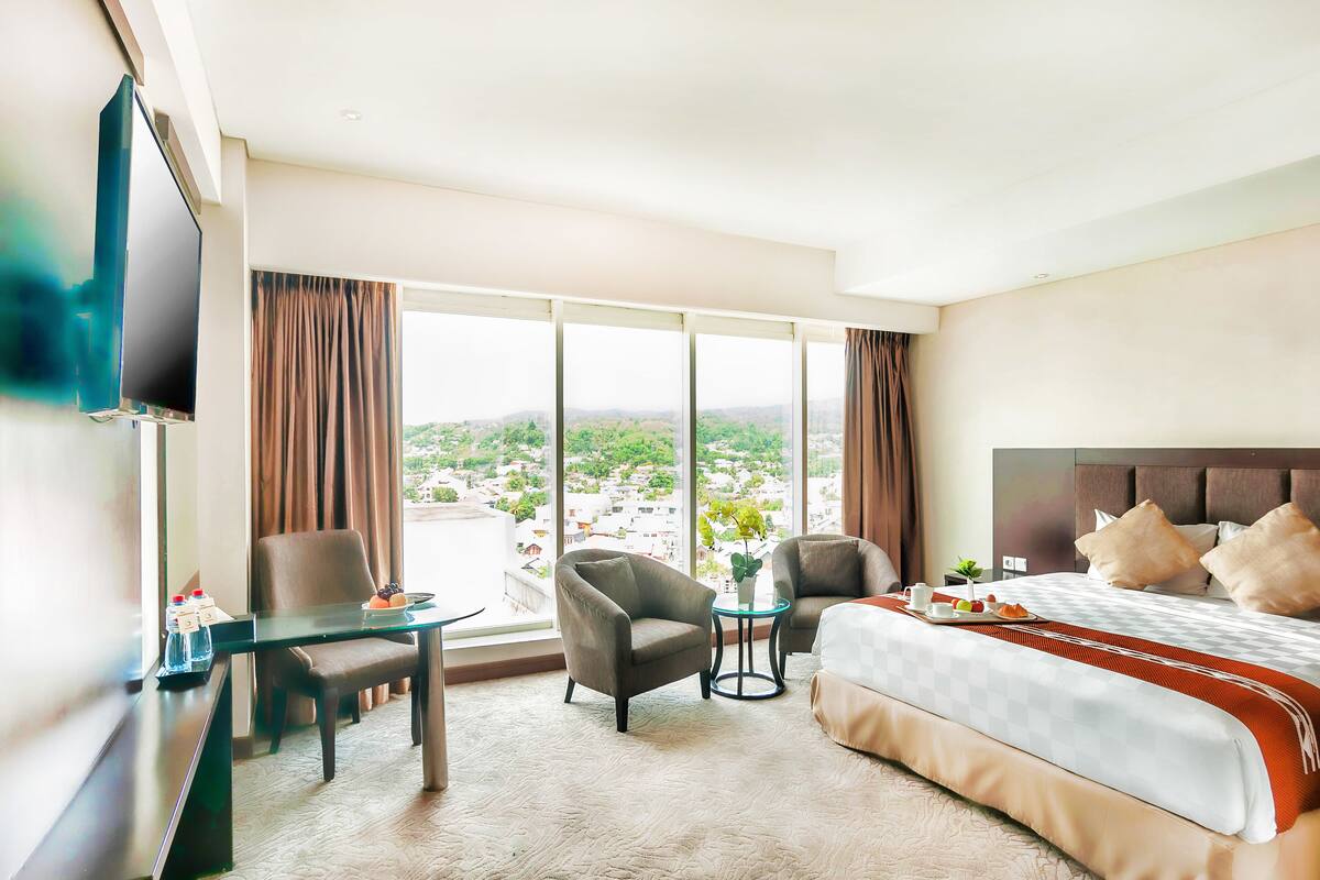 A hotel room with a large bed, two armchairs, a small table with a plant, and a TV on the wall.