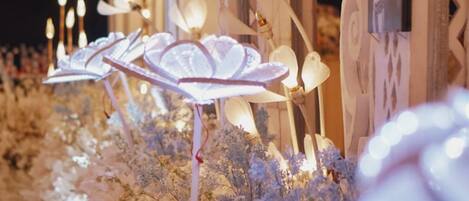 Un chemin bordé de compositions florales illuminées et de bougies, menant à une porte ornée d’un panneau décoratif.