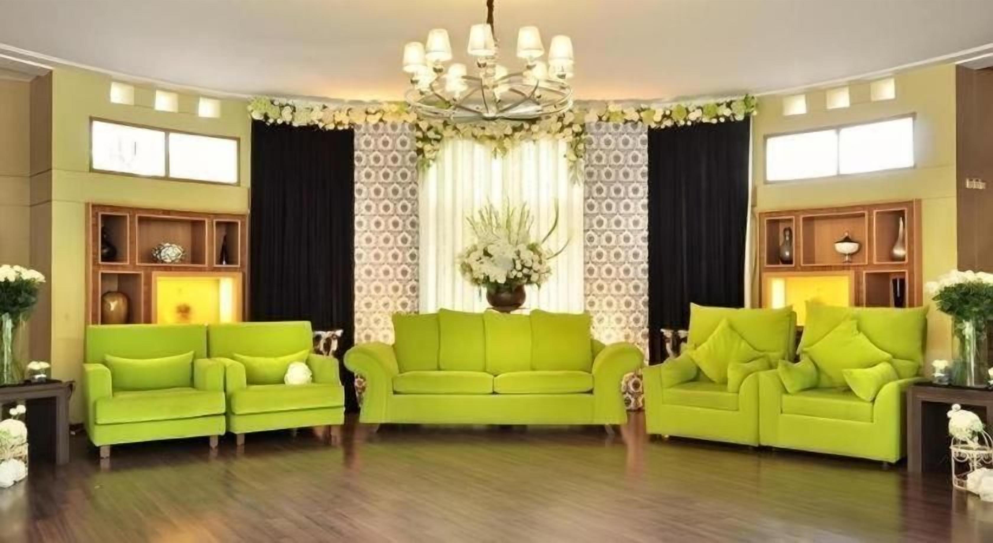 A living room with a green sofa set, a chandelier, and patterned wallpaper.