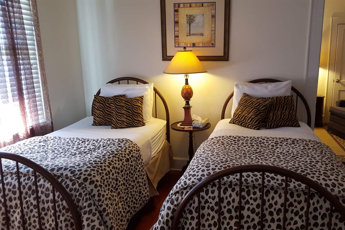 Une chambre d’hôtel avec deux lits simples, chacun recouvert d’une couvre-lit à motifs léopard, une table de chevet avec une lampe et un tableau encadré au mur.