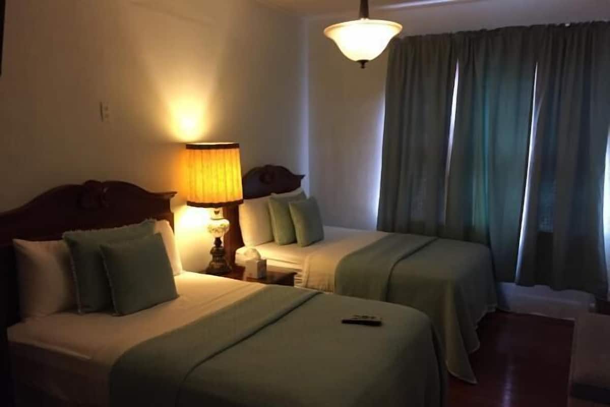 Une chambre d’hôtel avec deux lits, une table de chevet avec une lampe et une fenêtre avec des rideaux.