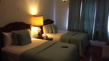 A hotel room with two beds, a nightstand with a lamp, and a window with curtains.
