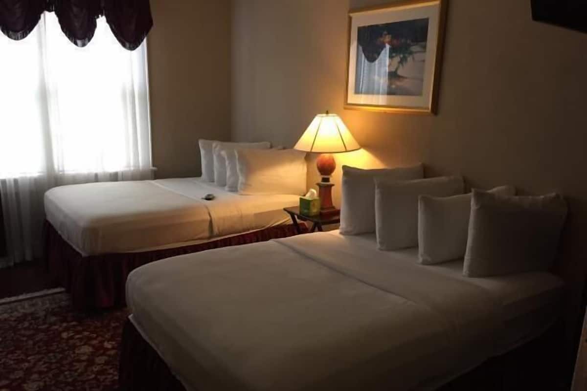 Une chambre d’hôtel avec deux lits simples, une table de chevet avec une lampe et un tableau encadré au mur.