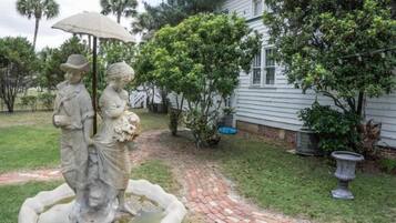 A garden with a statue, a brick pathway, and a house.