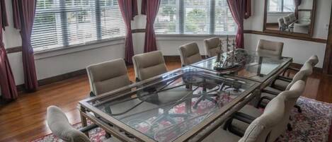 A conference room with a glass table, beige chairs, a chandelier, and large windows with curtains.
