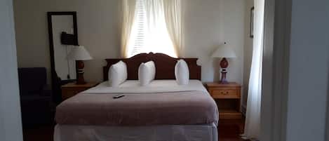 Une chambre d’hôtel avec un grand lit, deux tables de chevet avec des lampes, une fenêtre avec des rideaux et une chaise.