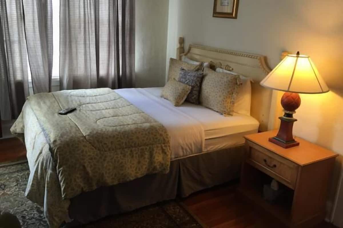 Un lit bien fait, recouvert d’une couvre-lit à motifs, une lampe de chevet et un tableau encadré au mur.