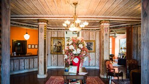Un hall con mostrador de recepción de madera, un jarrón rojo con flores y una araña.