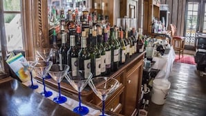 Zona de bar con una variedad de botellas y vasos, muebles de madera y vistas amplias a través de grandes ventanales.