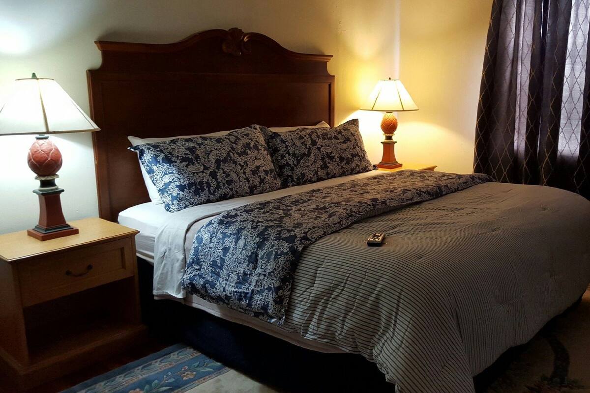 Un lit bien fait, recouvert d’une couvre-lit à motifs, avec deux lampes de chevet et une table de chevet en bois dotée d’un tiroir.