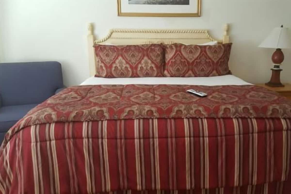Un lit recouvert d’une couvre-lit à motifs, une chaise bleue et une table de chevet avec une lampe.