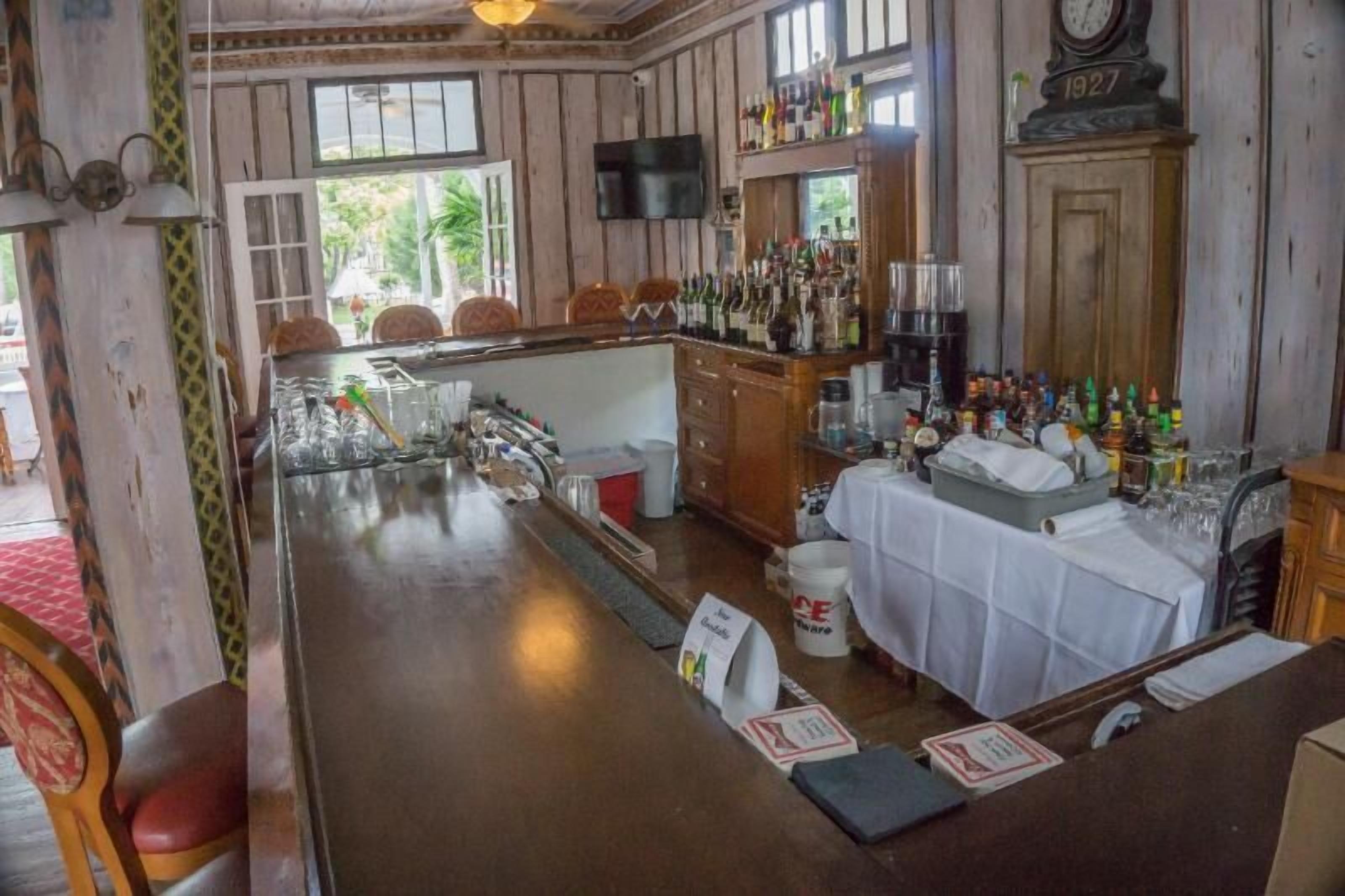 Eine Bar mit Holzwandverkleidung, einem an der Wand befestigten Fernseher und einer Auswahl an Flaschen und Gläsern auf Regalen.