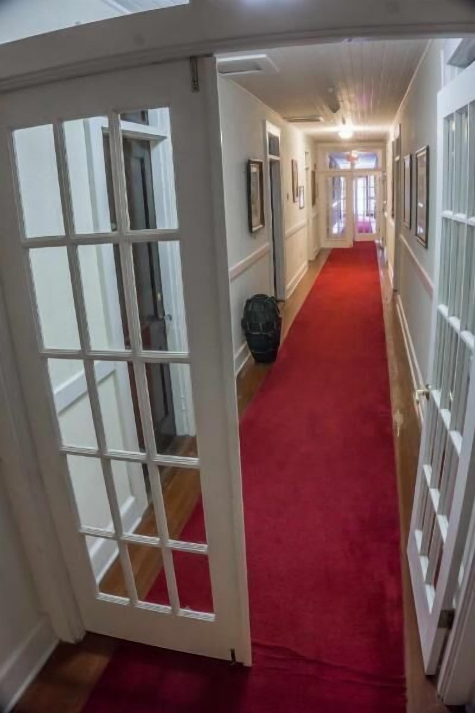 A hallway with a red carpet, white walls, and a door with a grid pattern.