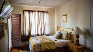 A bedroom with a bed, a nightstand, a lamp, a ceiling fan, a window with curtains, and a door.