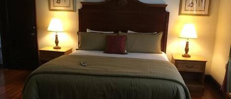 Una cama bien hecha con cabecera de madera, dos lámparas de noche y un cuadro con motivos florales.