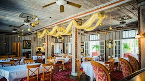 Un restaurante con mesas y sillas de madera, tela amarilla decorativa y piso cubierto de alfombra roja.