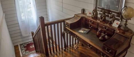 Una escalera de madera con barandilla que lleva a una habitación con un espejo grande, un globo terráqueo y un escritorio con cajones.