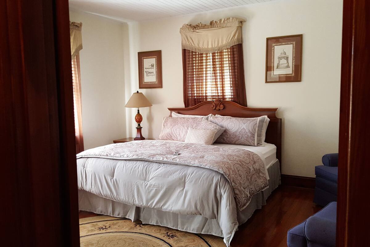 Une chambre à coucher avec un grand lit, une table de chevet, une lampe et deux tableaux encadrés accrochés au mur.
