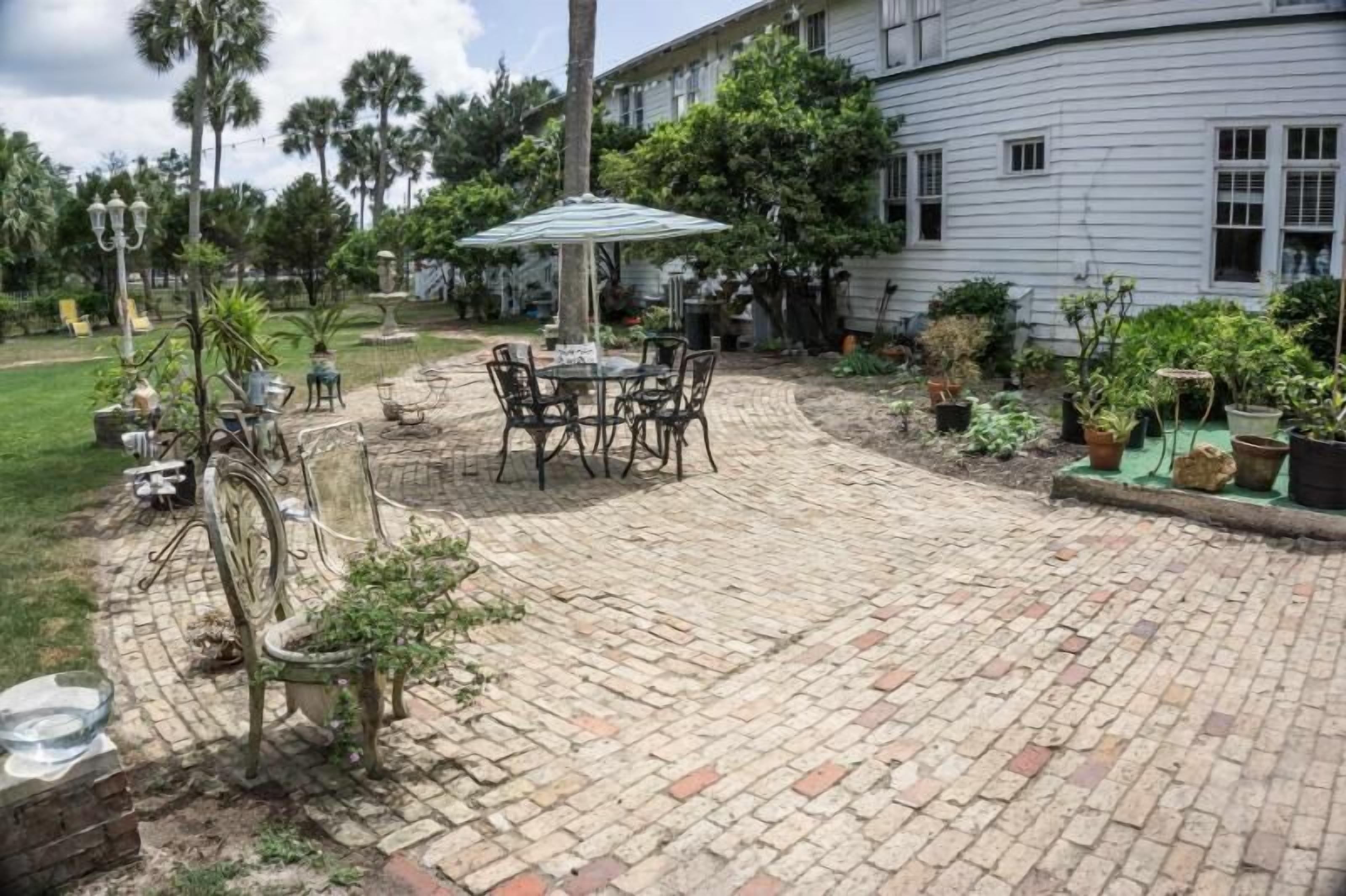 Un patio con una mesa y sillas, rodeado de plantas en macetas y un suelo de ladrillo.