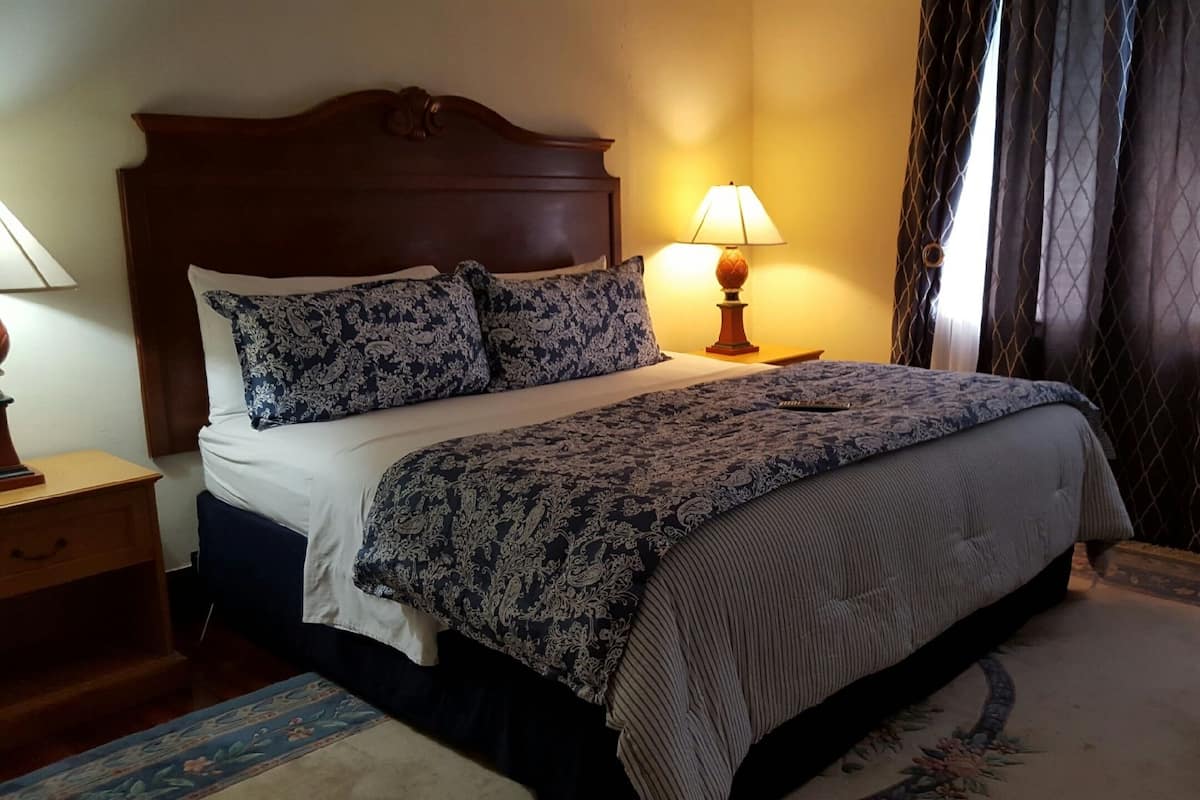 Un lit bien fait, avec une literie à motifs, une tête de lit en bois, une lampe de chevet et un tapis à fleurs.
